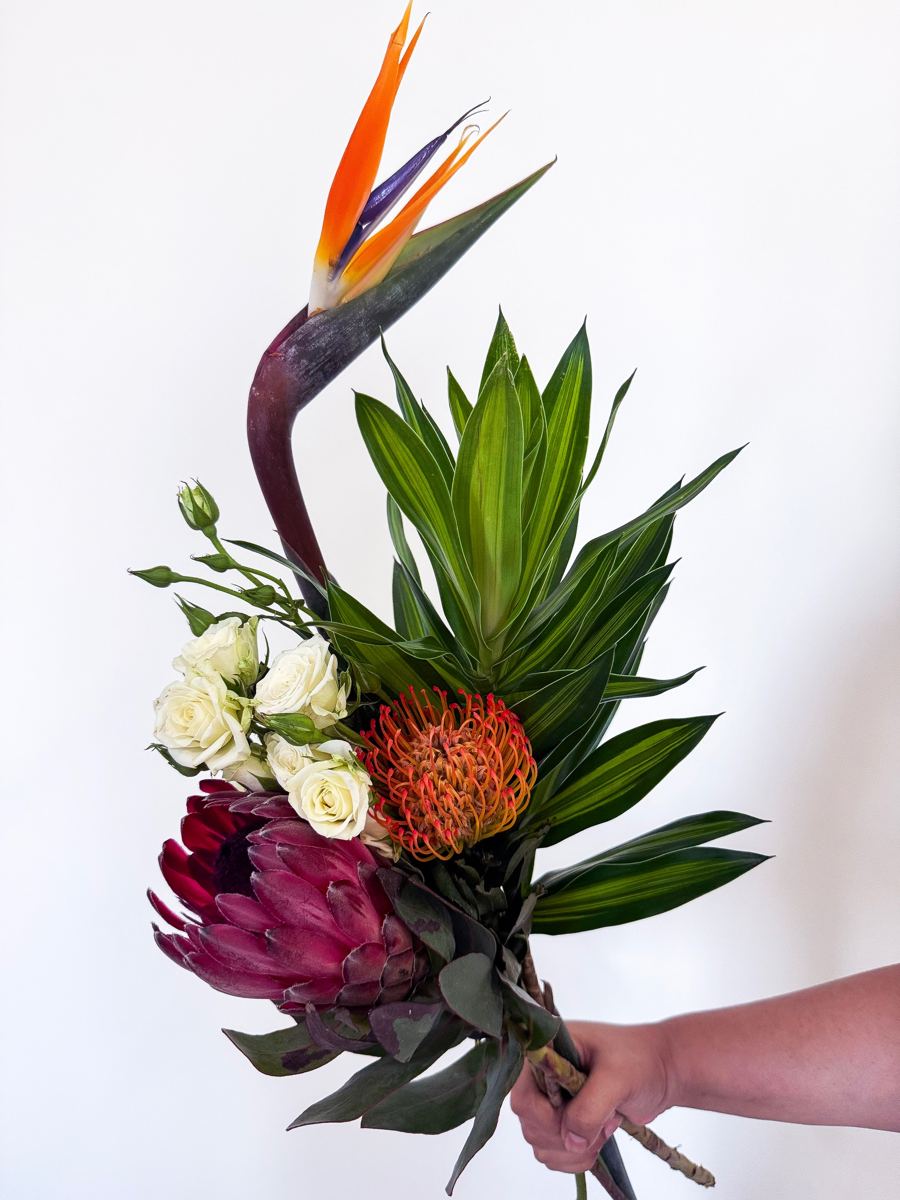 Bird of paradise, king protea, pincushion protea and cream spray roses with tropical leaves